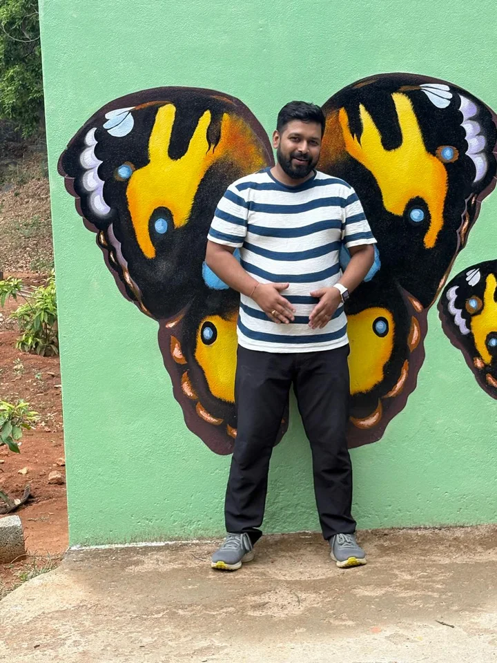 Mrinal in a striped t-shirt, standing in front of a painted pair of butterfly wings